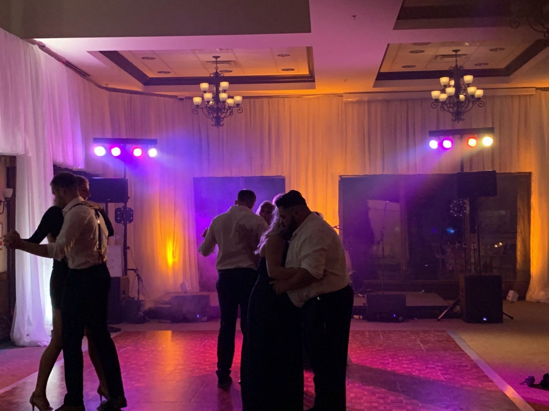 People dancing in a brightly lit ballroom. Purple and orange stage lighting.