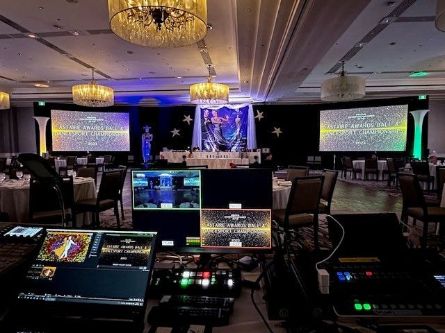 Event setup with stage, screens, tables, and lighting control equipment.
