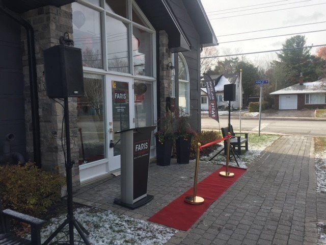 Exterior of a business with a red carpet, speaker, podium, and a building with large windows.