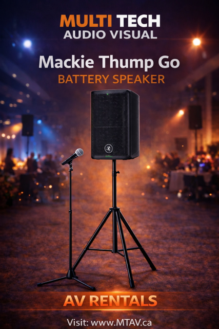 Mackie Thump Go battery speaker on a stand with a microphone. Background is an event with warm lighting.