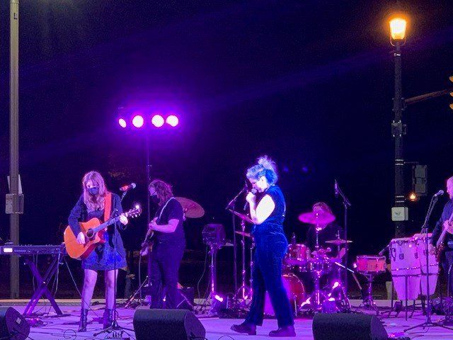 Band performing on an outdoor stage at night, lit with purple lights.