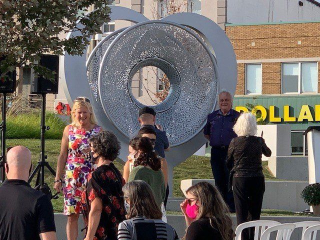 People gather near a large, abstract metal sculpture shaped like a heart in front of a Dollarama store.
