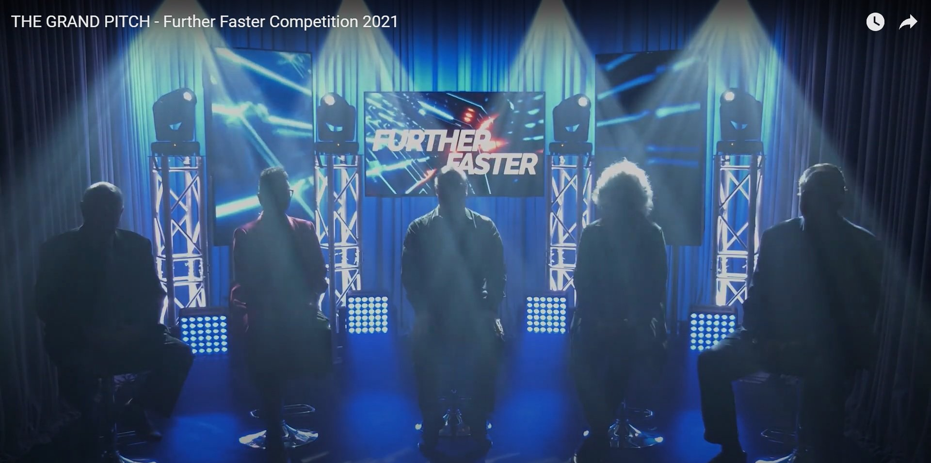 Judges on stage, blue lighting and background, the words 