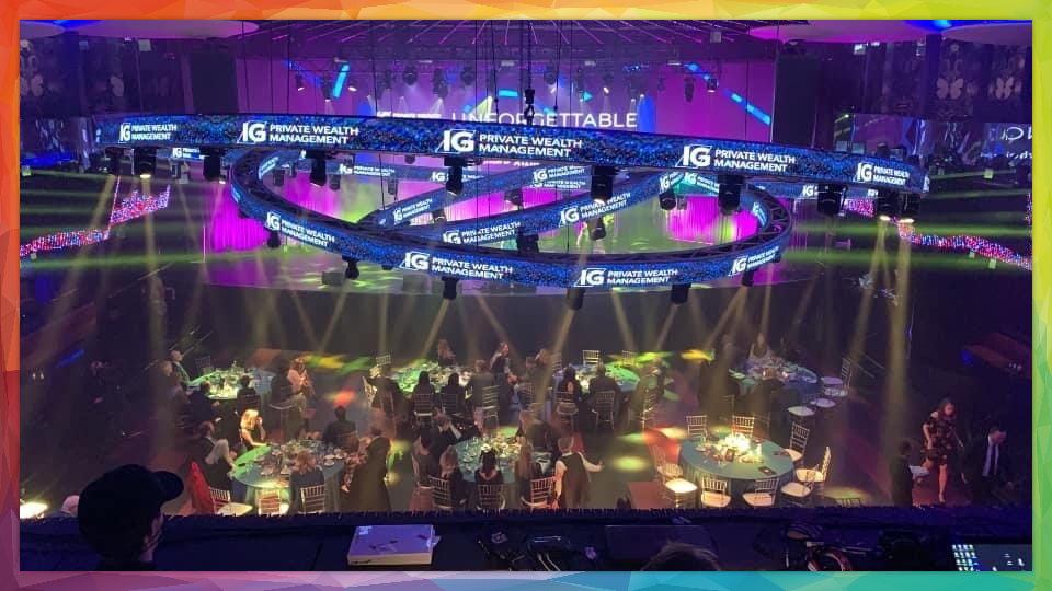 Event stage with a band performing; overhead LED rings; tables with guests.