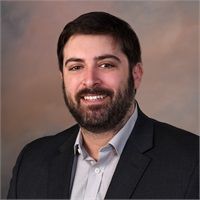 A man with a beard is wearing a suit and smiling for the camera.