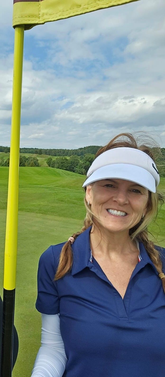 A woman wearing a visor and a blue shirt is standing on a golf course.