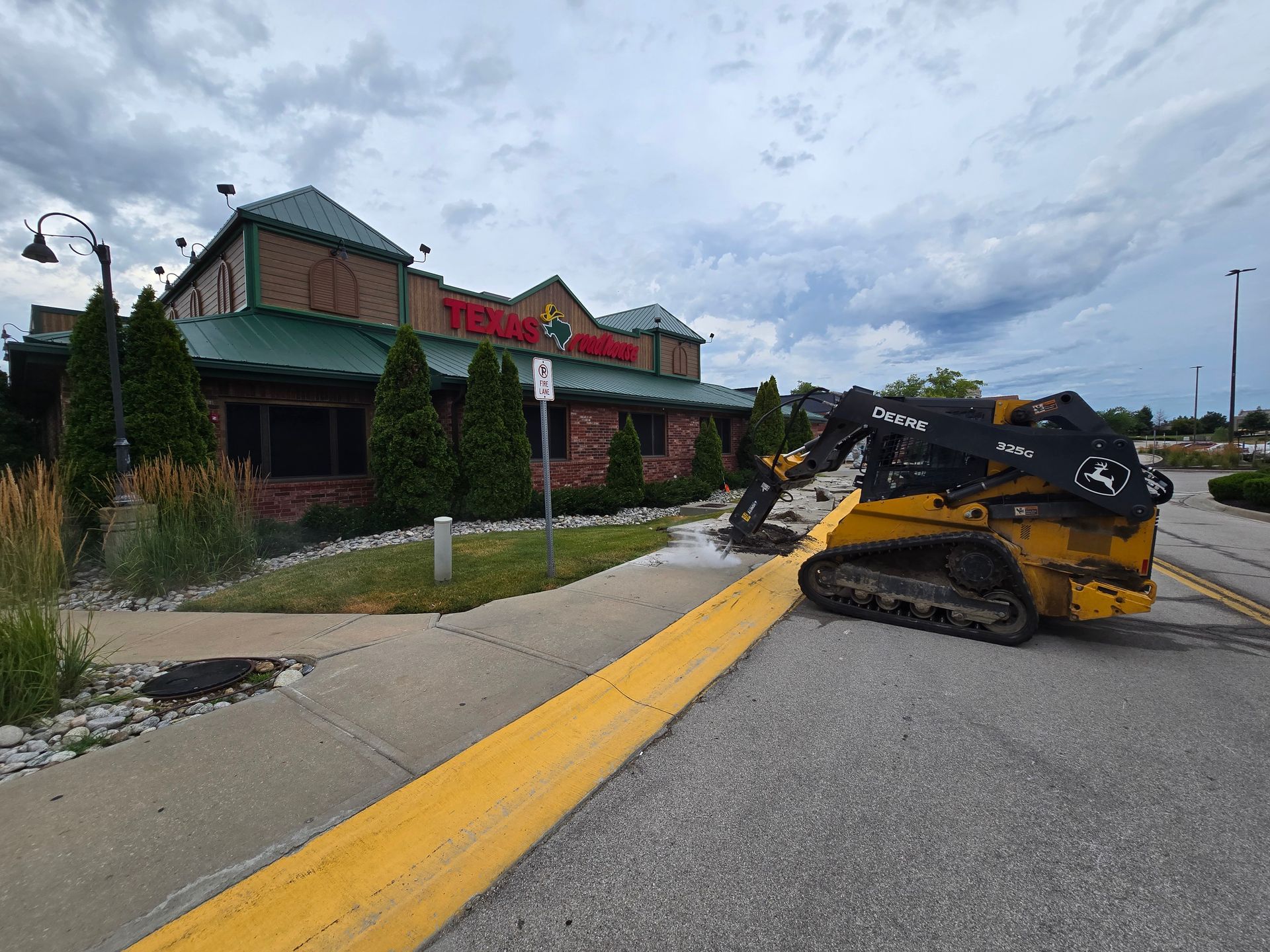 Tracked skid steer on road working on a concrete walkway of a commercial building