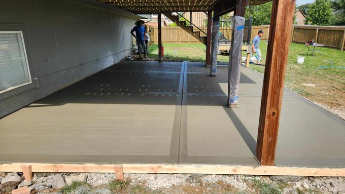 Covered concrete patio under construction, with a worker near the back and wooden posts supporting the roof