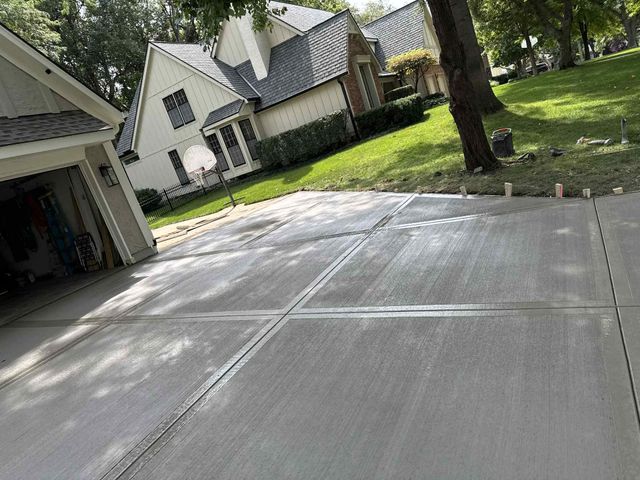 Tilted view of a concrete driveway beside a garage, with suburban houses and green lawn in the background