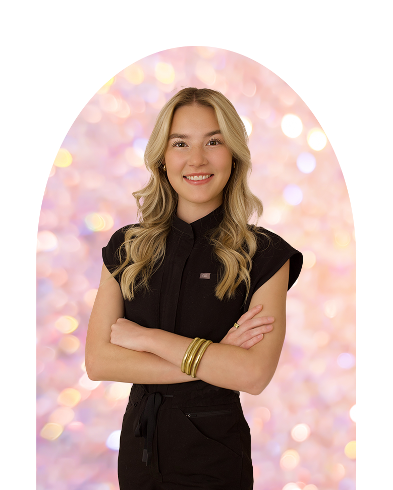 A woman in a black dress is standing with her arms crossed and smiling.