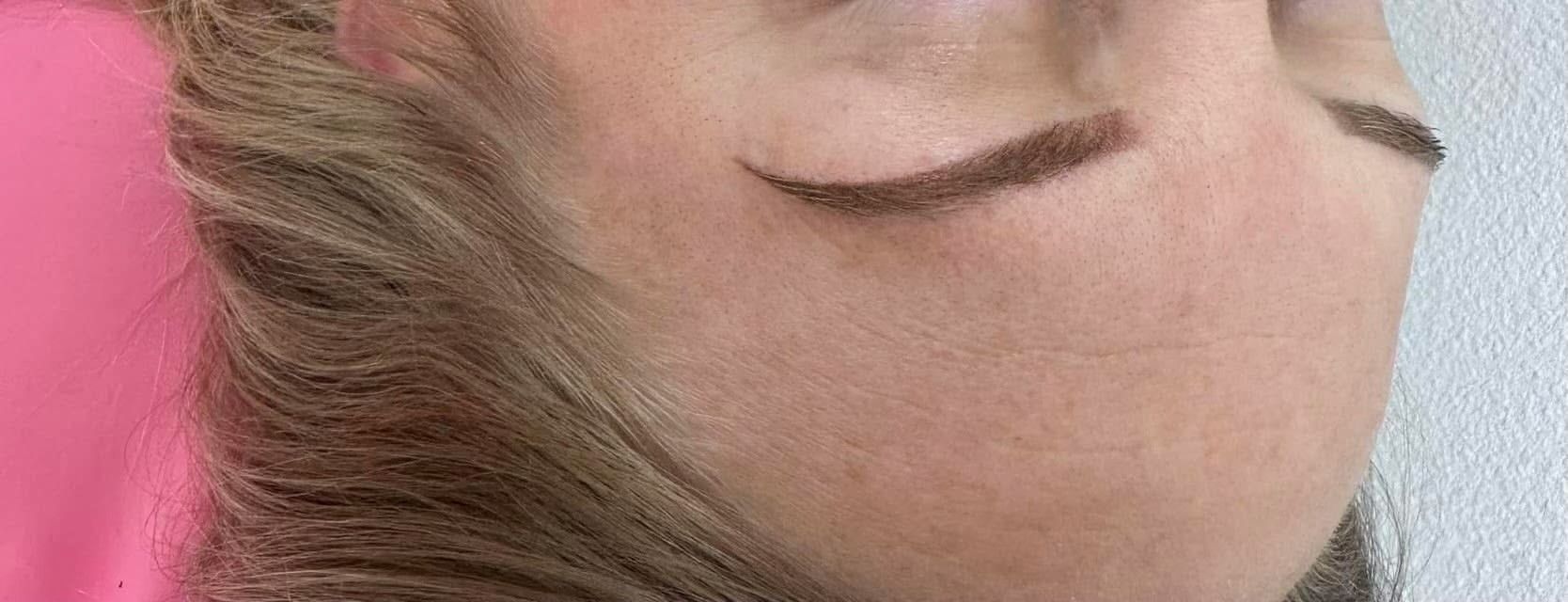 Close-up of a person's face with a brown eyebrow. The skin is pale and there is hair.