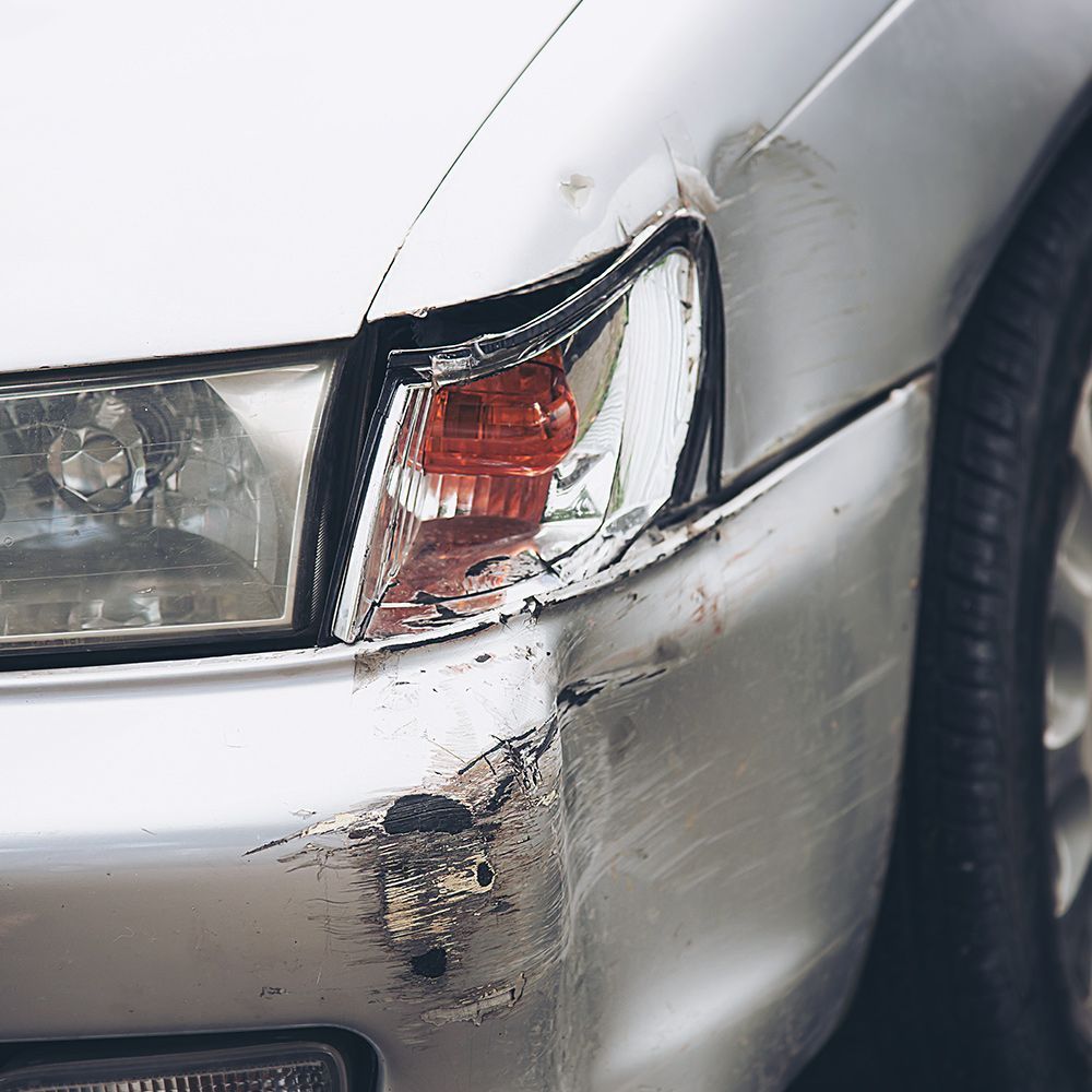 A silver car with a damaged bumper and headlight