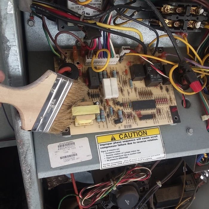 A person is using a brush to clean the circuit board of an AC unit.