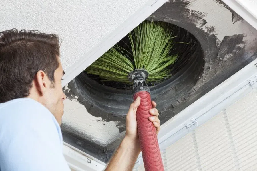 Man cleaning air duct with rotating brush tool in ceiling.