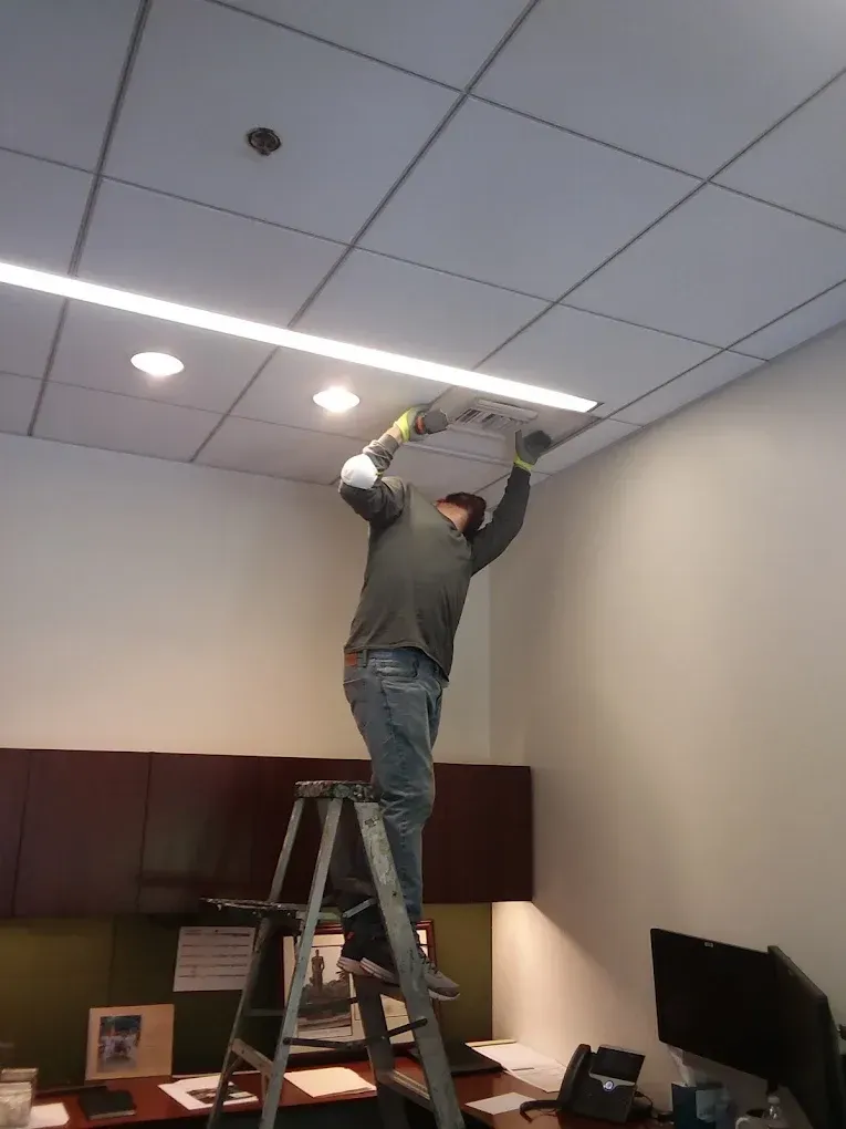 Man on ladder installing a ceiling light in an office.