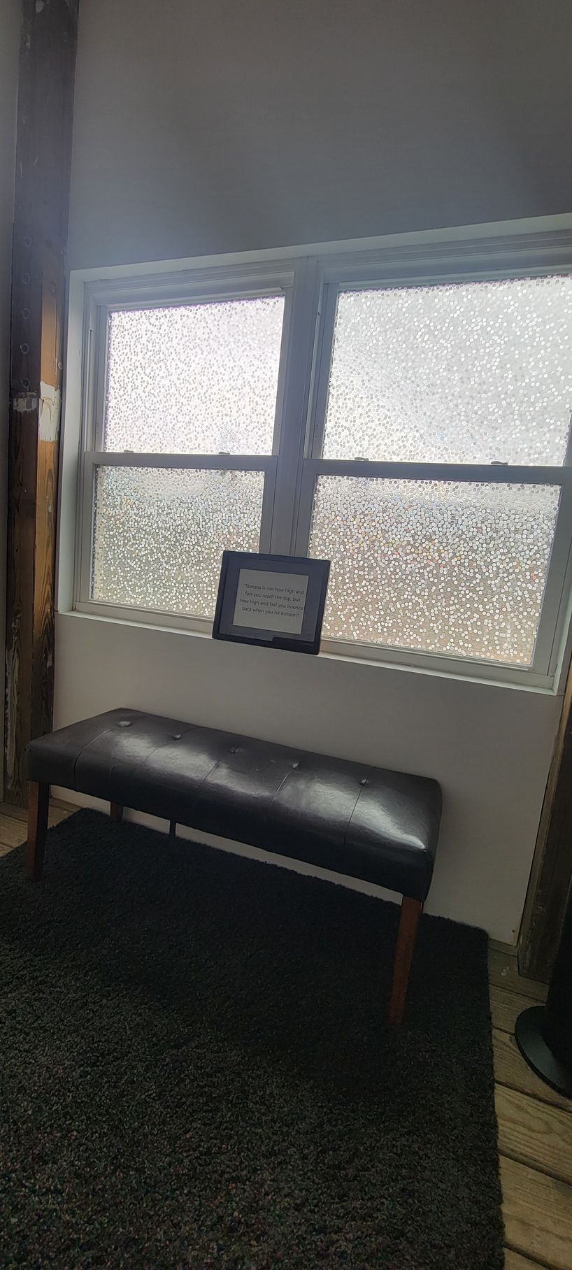 Small waiting area with a black bench beneath a frosted window and a framed item on the sill.