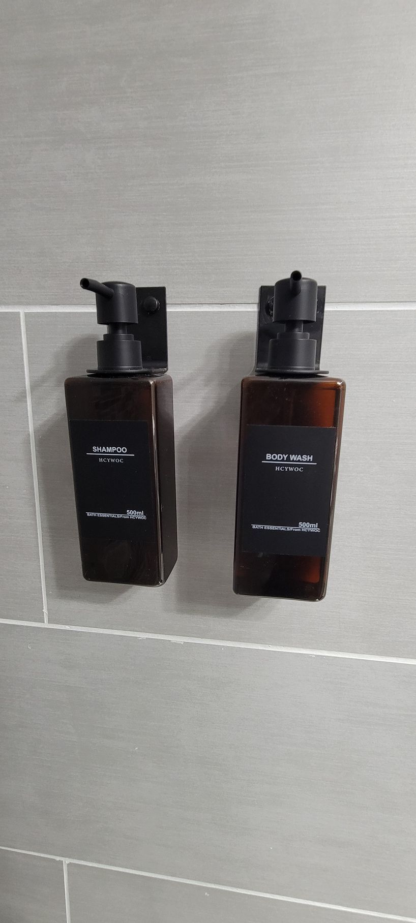 Two brown pump bottles mounted side by side on a light gray tiled wall.