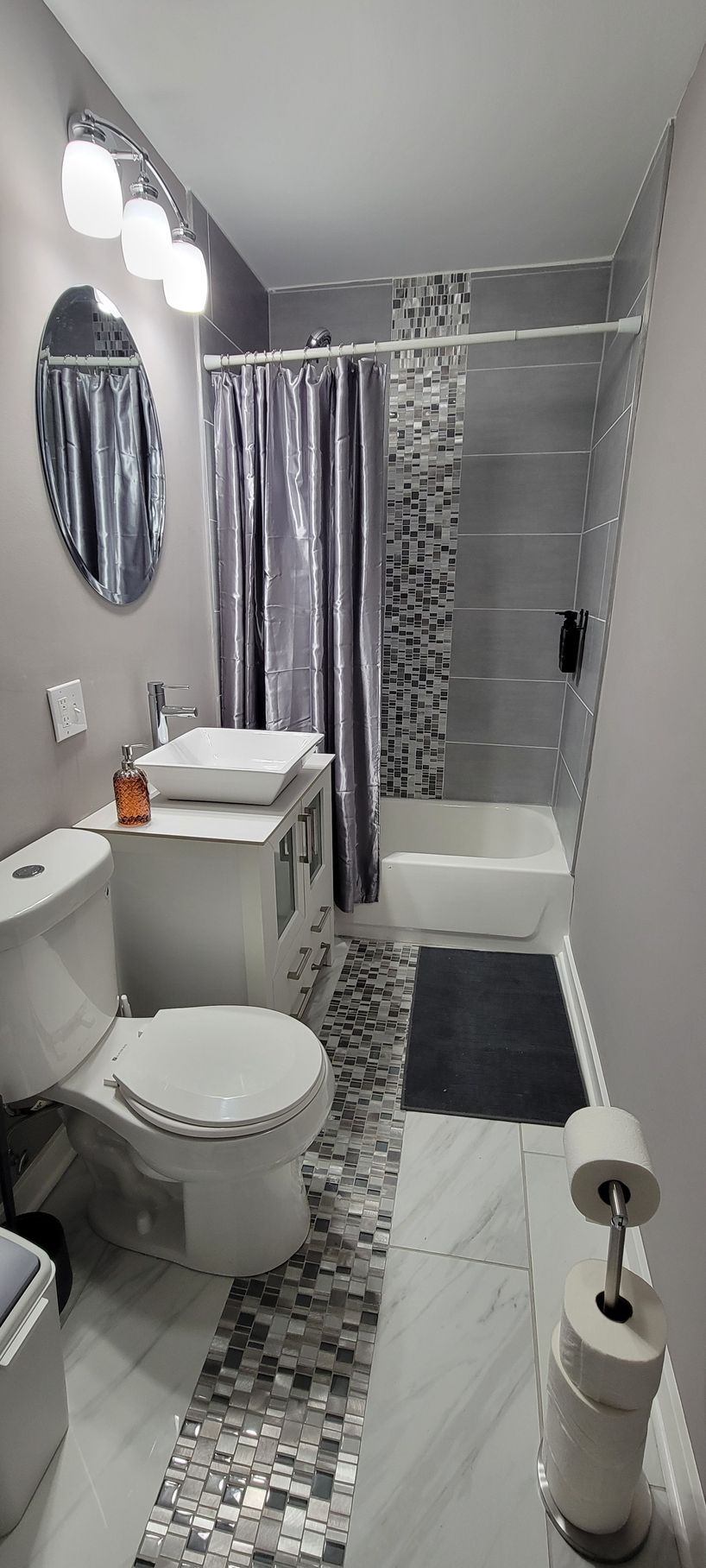 Narrow bathroom with toilet, sink, shower curtain, and gray-black mosaic tile floor.