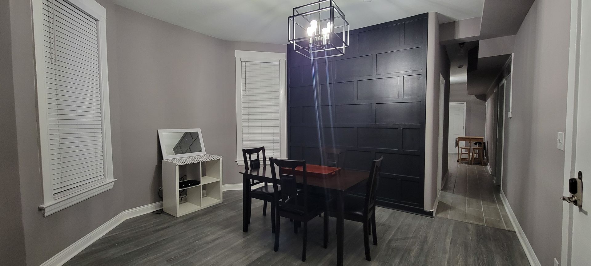 Dining room with black table and chairs, dark cabinet wall, gray floors, and a chandelier.