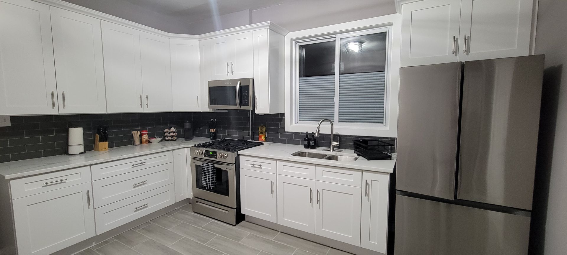 Modern white kitchen with stainless steel appliances, window over the sink, and black countertop appliances