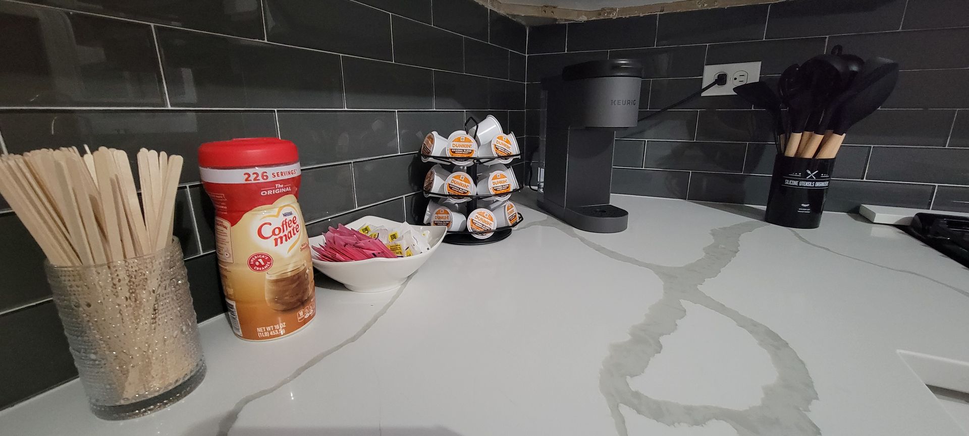 Coffee station with cups, stirrers, a container of creamer, and a drip coffee machine on a counter.
