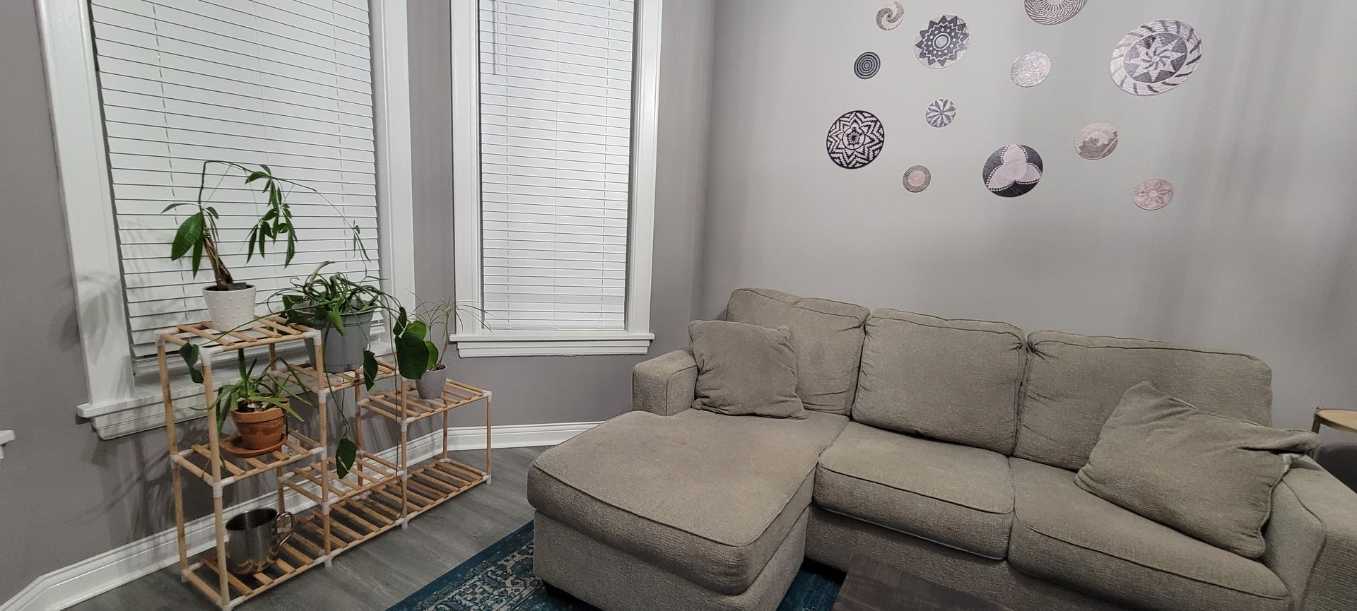 Cozy living room with a beige sectional, potted plants on a shelf, and decorative wall decals by the windows.