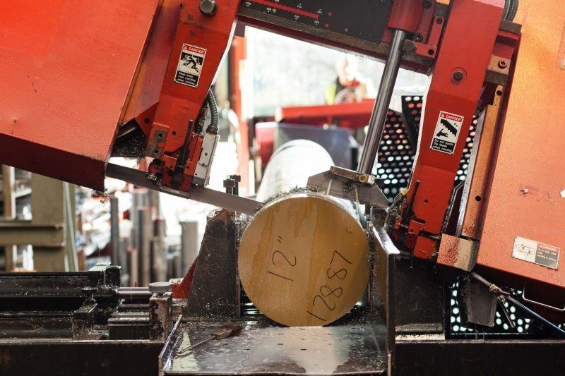 Industrial saw cutting a large metal log in a workshop