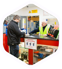 Customer at a shop counter talking to a clerk in a black jacket and yellow vest