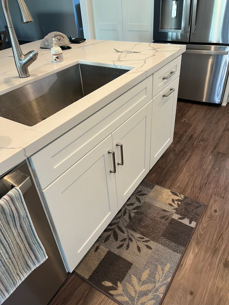 A kitchen with white cabinets , stainless steel appliances , a sink and a rug.