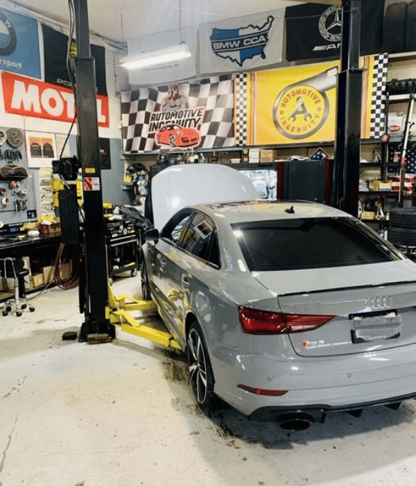 Silver Audi sedan positioned on a lift inside an automotive repair shop.