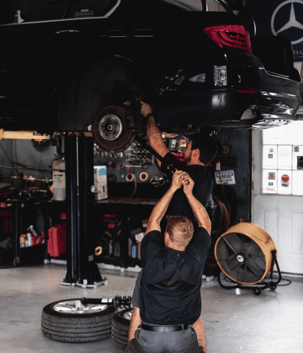 Two mechanics under a lifted black car