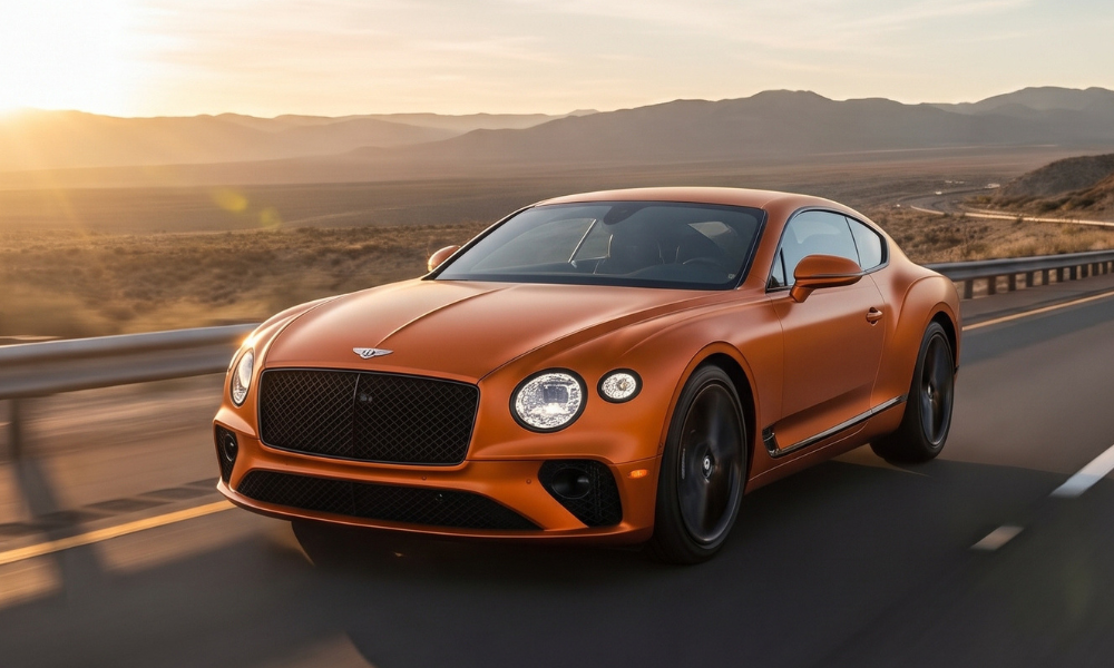 Orange Bentley Continental GT luxury grand touring coupe driving along a desert highway at golden hour, with mountains and open desert landscape behind it