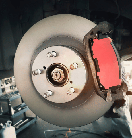 Close-up of a vehicle brake rotor and red brake pad with the wheel removed.