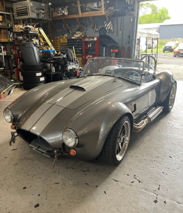 Gray classic roadster parked inside an automotive repair shop.