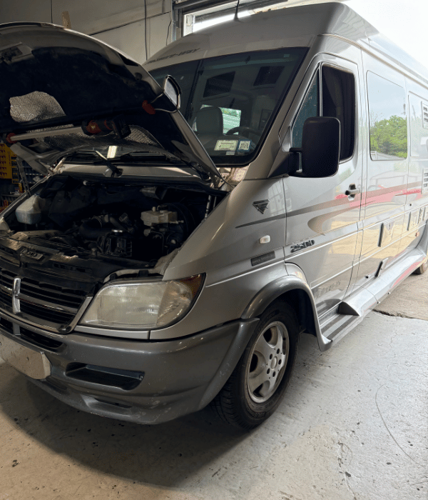 Mercedes-Benz Sprinter van with its hood open inside an automotive repair shop.