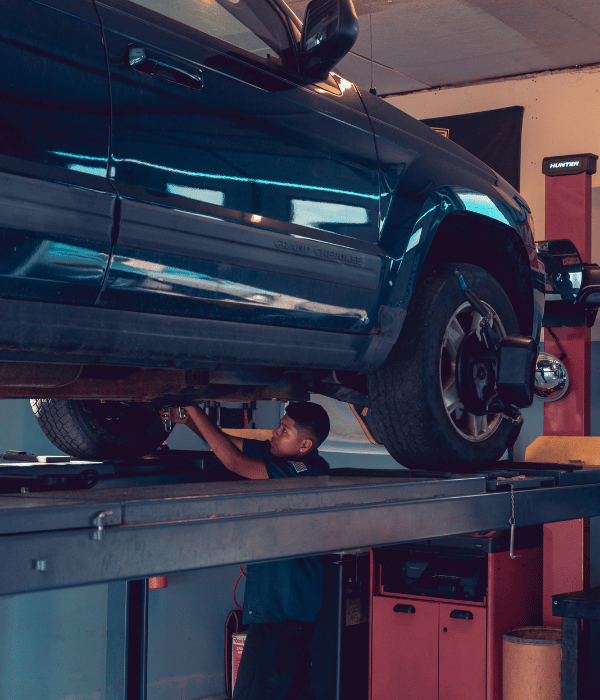 Technician working underneath a Jeep Grand Cherokee raised on an automotive lift.