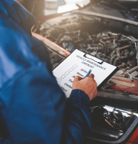 Automotive technician completing a vehicle maintenance checklist beside an open engine bay.