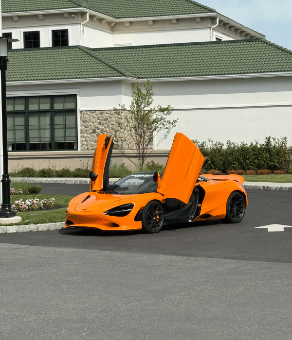 Orange McLaren sports car with its doors raised outside a building.