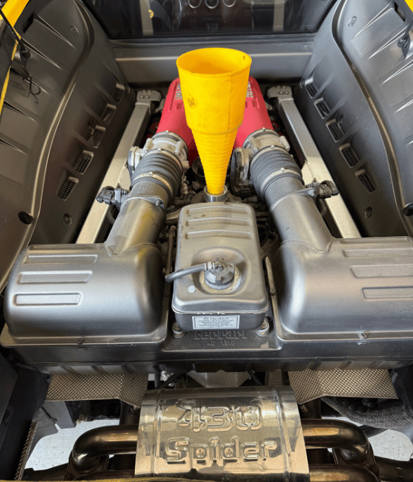 Engine oil being added through a funnel in a Ferrari engine bay.