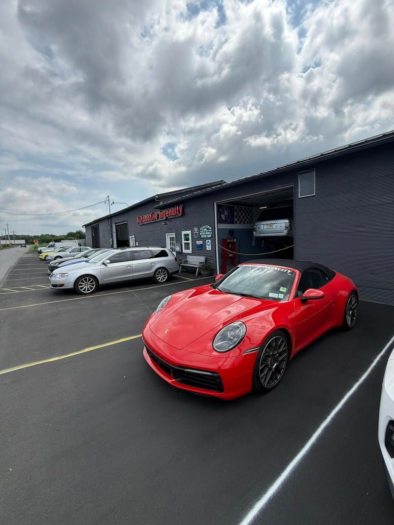 Red sports car parked outside the Automotive Ingenuity shop under a cloudy sky