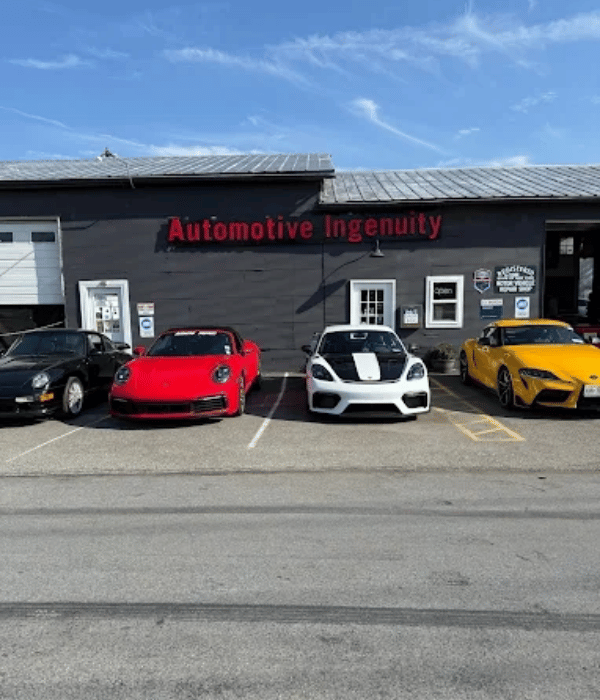 Automotive Ingenuity repair shop exterior with Porsche sports cars and a Toyota Supra parked out front.