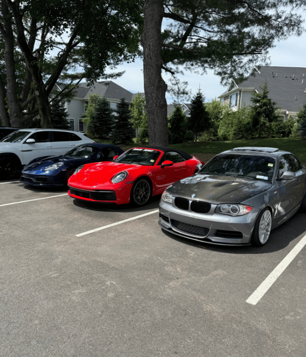 Red Porsche convertible and gray BMW coupe parked alongside other performance vehicles.