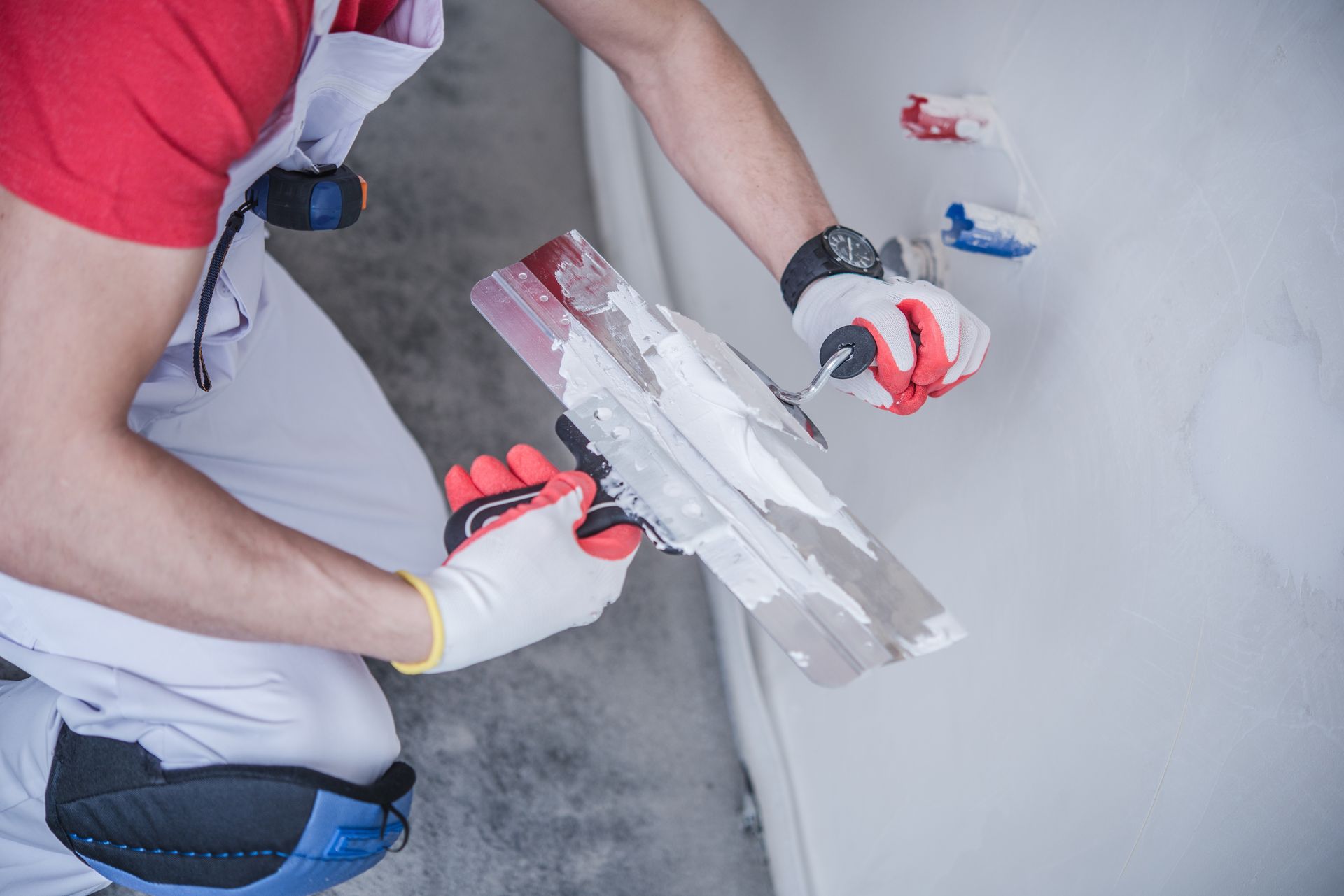 Person applying plaster to a wall with a trowel, wearing gloves and work clothing.