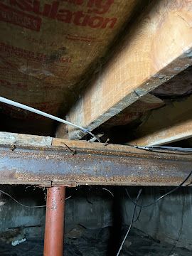 Exposed wooden beams and rusted metal supports in a crawl space or basement ceiling area