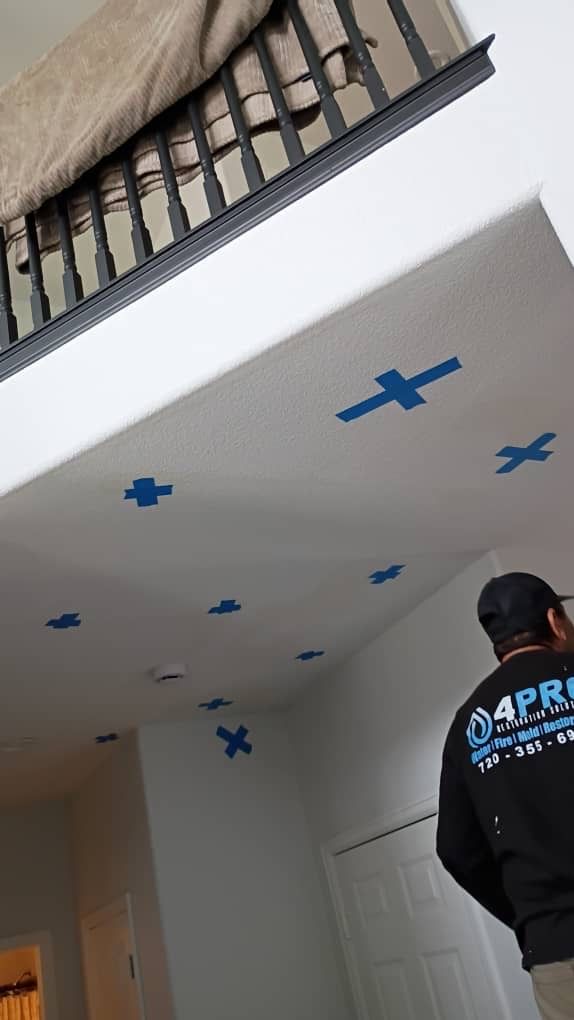 Person in a black hoodie standing in a room with blue painter’s tape markers on the ceiling and a staircase above.