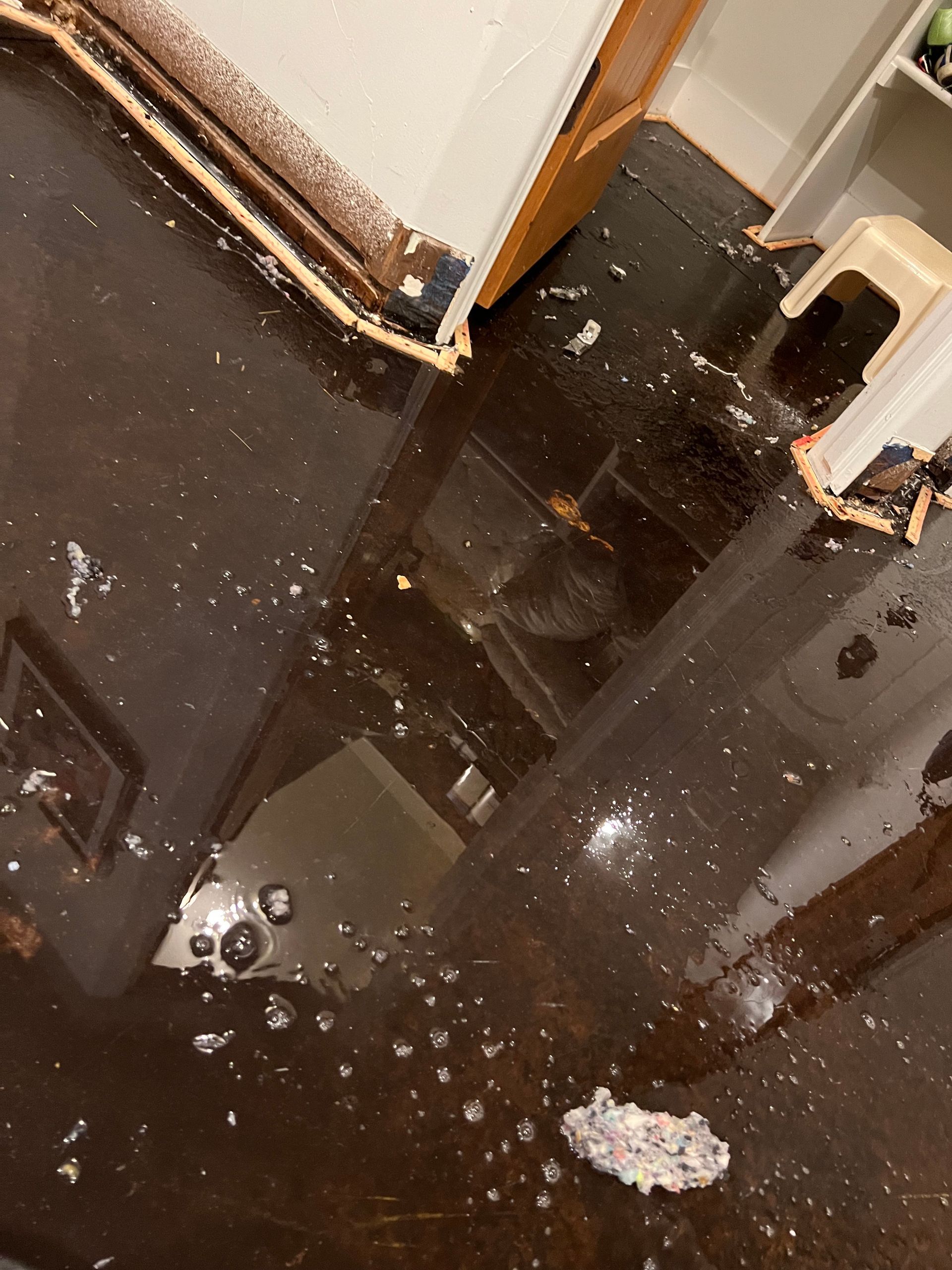 Spilled dark liquid with broken glass shards on a floor near a doorway and wall.