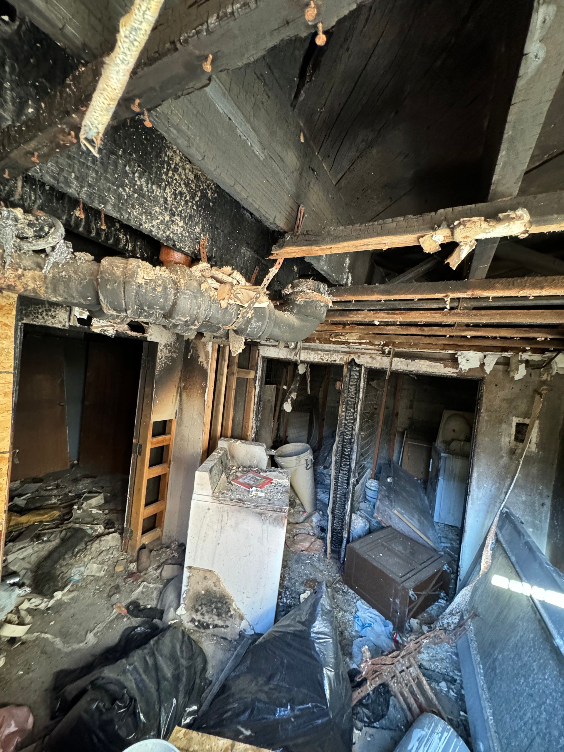Burned-out room with charred ceiling, debris, exposed beams, and a damaged doorway