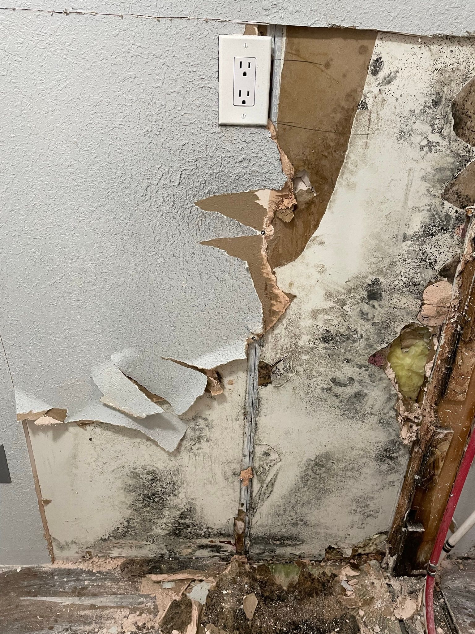 Damaged wall with peeling drywall and exposed insulation beneath a white outlet.