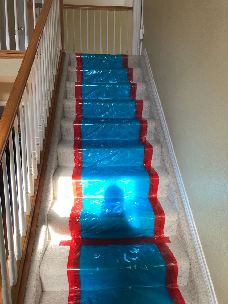 Blue plastic sheet covering carpeted stairs with red tape along the sides in a hallway.
