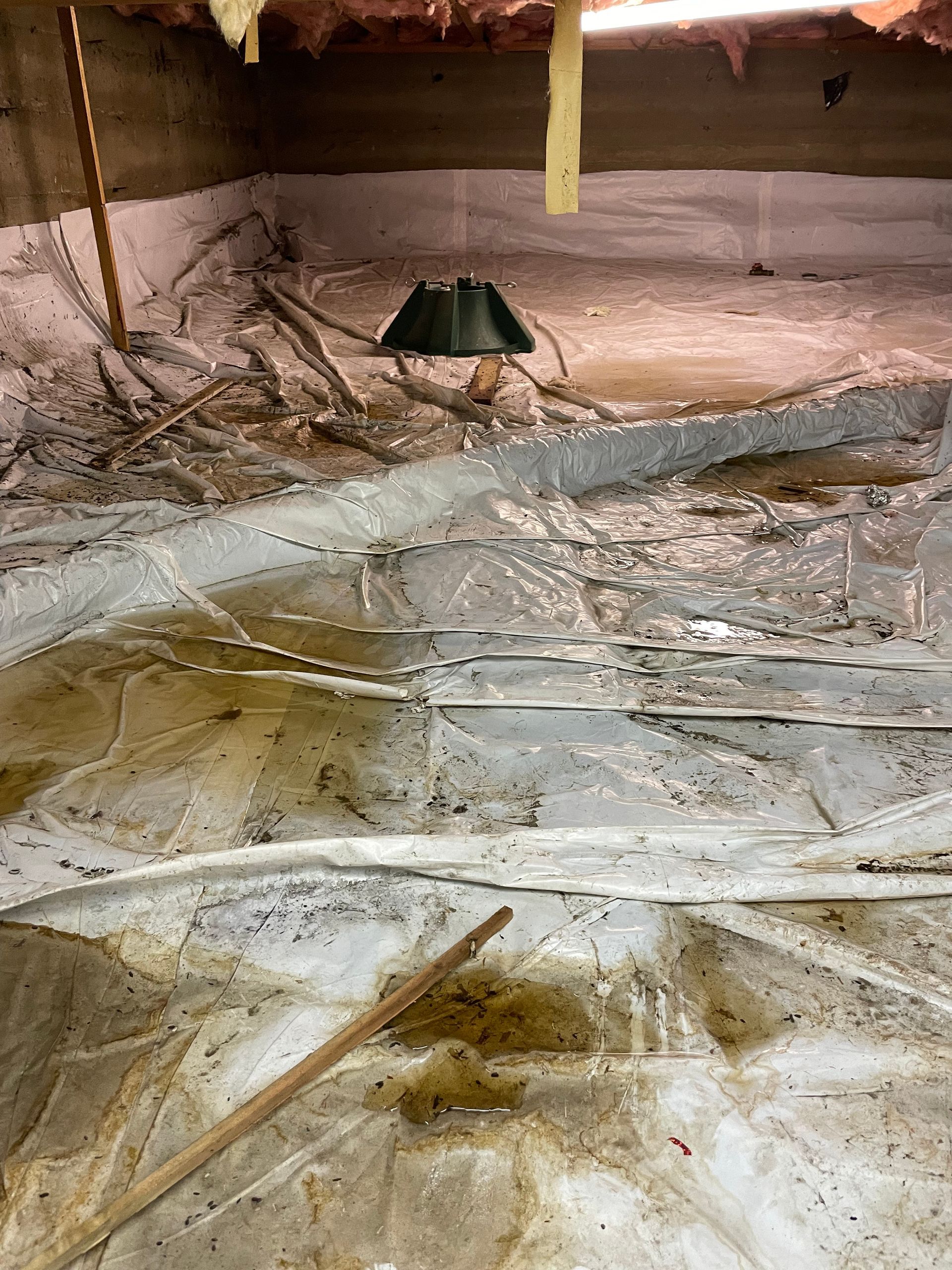 Crawlspace floor lined with plastic sheeting, exposed beams, and a small black device in the center